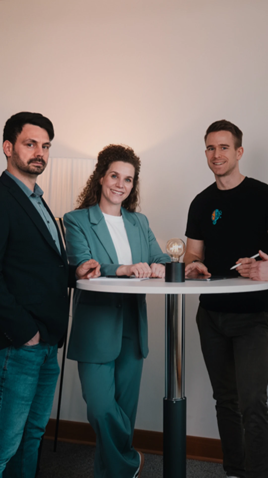Von Links: Florian Bobek, Lorena Tippelt, Dr. Florian Imgrund und Konstantin Auffinger. Sie stehen um einen Stehtisch auf dem sich eine Lampe befindet. Links neben den Personen steht eine Pflanze.