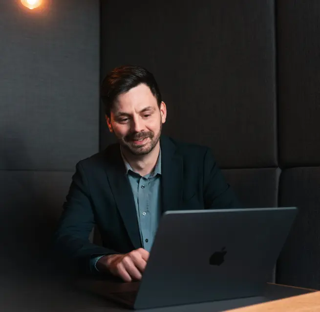 Florian Bobek sitzt an einem Tisch. Auf dem Tisch steht ein Laptop, in den Herr Bobek schaut.