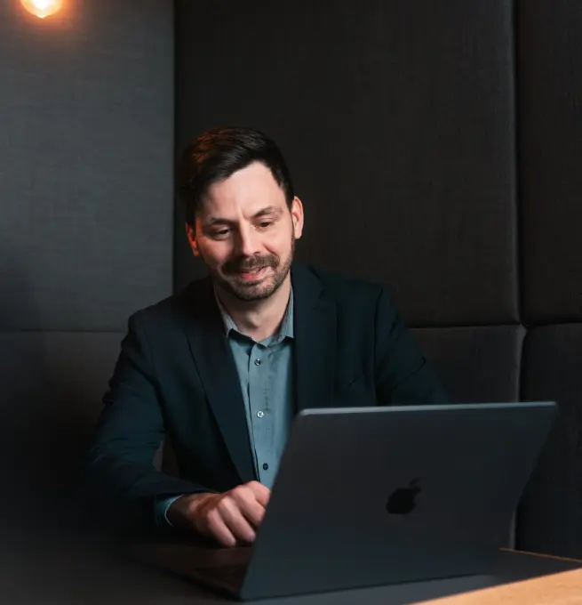 Florian Bobek sitzt an einem Tisch. Auf dem Tisch steht ein Laptop, in den Herr Bobek schaut.
