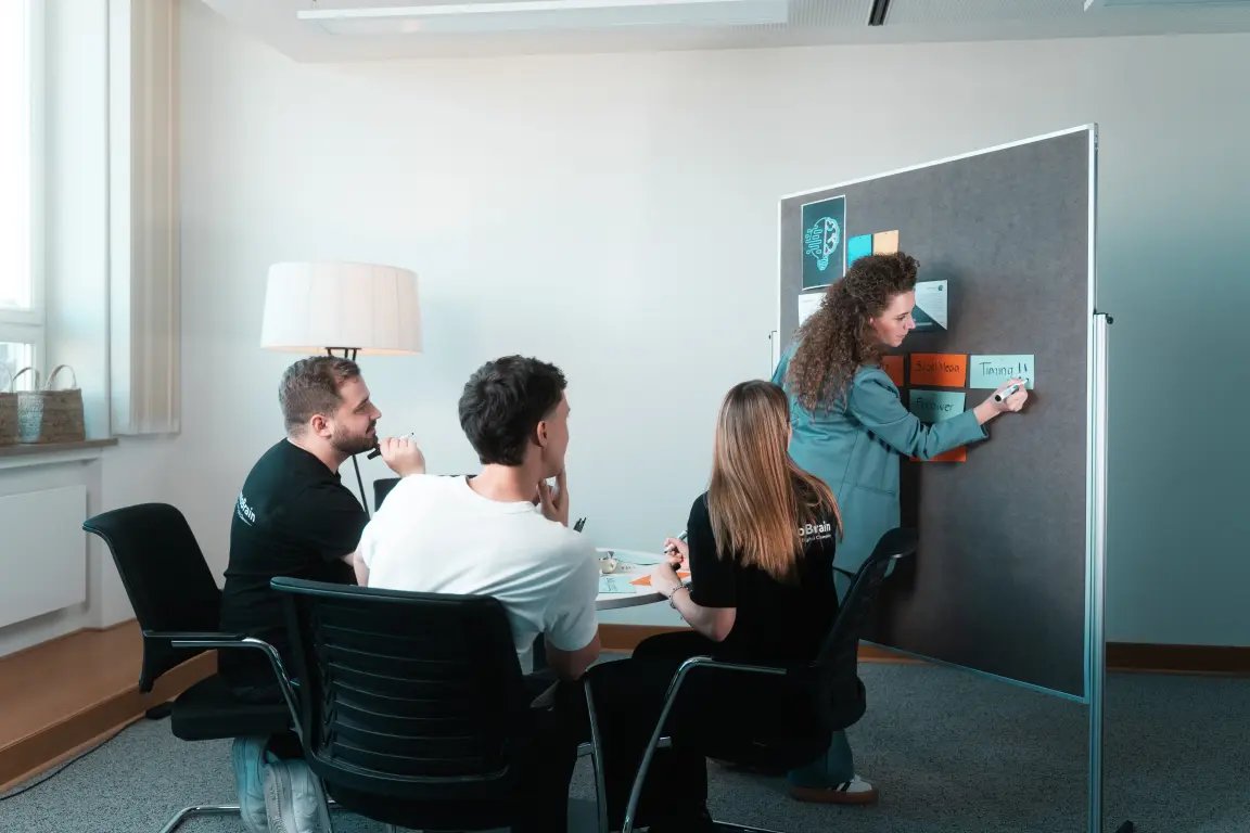 Tobias Reuß, Lorena Tippelt, Tim Ebel und Emma Martin bei einer Besprechung. Lorena schreibt gerade etwas an das Clipboard.