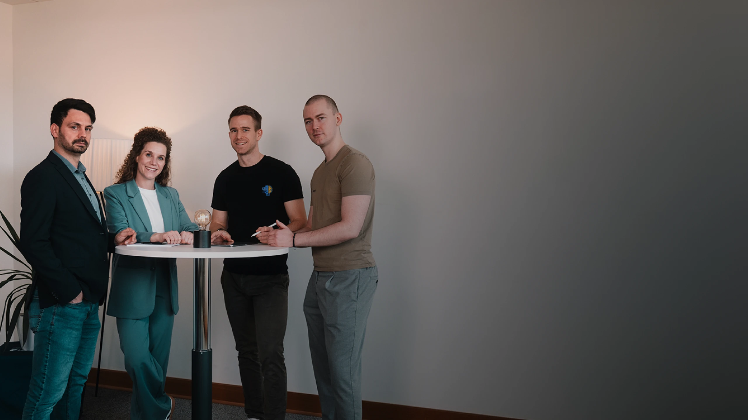 Von Links: Florian Bobek, Lorena Tippelt, Dr. Florian Imgrund und Konstantin Auffinger. Sie stehen um einen Stehtisch auf dem sich eine Lampe befindet. Links neben den Personen steht eine Pflanze.