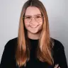 Emma Martin in einem Portraitformat. Sie trägt eine Brille, verschränkt ihre Arme und hat zwei Perlenketten am Handgelenk.